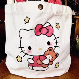 Söt liten tote bag med Hello Kitty-motiv! - Söt liten tote bag i canvas med knäpp-knapp och Hello Kitty-motiv. Mått: 25 x 27 cm. Oanvänd.