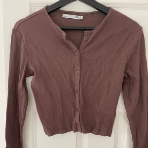 Brun ribbad topp från 157 - Säljer en brun ribbad topp från 157 med lång ärm och knappar framtill. Modellen är croppad och har en rund halsringning.❤️