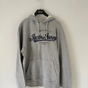 Grå hoodie från Jack & Jones - Säljer en grå hoodie från Jack & Jones med tryck framtill. Tröjan är helt ny men passade bara inte helt enkelt, storleken är S men borde även passa XS! Pris går att diskuteras😀