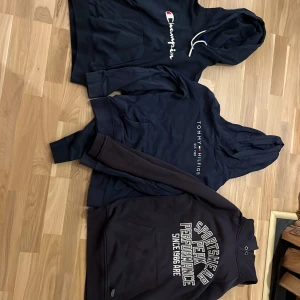 Hoodie - Säljer en mörkblå hoodie från Champion med stor logga broderad på bröstet. Tröjan har huva med vita snören, känguruficka och ribbade muddar. Perfekt för dig som gillar sportig och avslappnad stil. En tommy och en peak. Peak Goodwin har ett litet riv hål på insidan av ärmen som man inte ser eller märker av skriv om ni vill ha bild på det. Storlek S/M