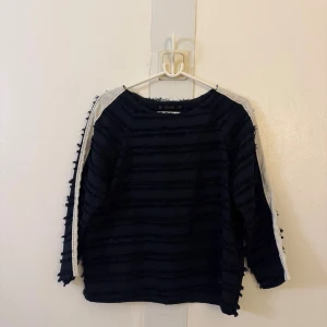 Svart tröja med fransiga ränder och vit detalj - Cool svart tröja från Zara med fransiga horisontella ränder och en vit rand längs ärmarna. Tröjan har lång ärm och en lite boxig passform. Perfekt för dig som gillar unika detaljer och en trendig look. Passar både S och M!