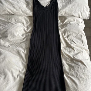 Svart ribbad långklänning - Snygg svart midiklänning med ribbad struktur och v-ringad hals. Klänningen har en smickrande, kroppsnära passform. Perfekt för dig som gillar stilrena och minimalistiska plagg med en modern touch.
