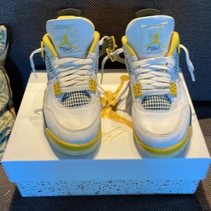 Nike Air Jordan 4 Tour Yellow - Nike Air Jordan 4 Retro 'Tour Yellow' med vit ovandel i skinn, gula och grå detaljer samt meshpaneler på sidorna. Klassisk Jumpman-logga på plösen och hälen. Skorna har snörning och en robust sula med synlig Air-enhet. Perfekta för dig som vill sticka ut med en ikonisk sneaker.