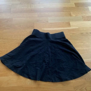 Svart kortkjol  - Svart kjol med bred resår i midjan och utsvängd form. Kjolen är kort och har ett mjukt material. 