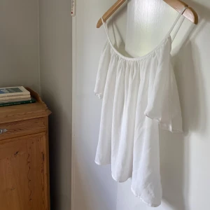 Vit offshoulder blus med tunna axelband - Superfin vit offshoulder blus med tunna axelband och vida, luftiga ärmar. Tyget är lätt och har en snygg fallande effekt. Perfekt för en fräsch och stilren look. Passar dig som gillar en luftig och avslappnad vibe. Var tvungen att klippa av lappen då den kliade. Storlek S/M