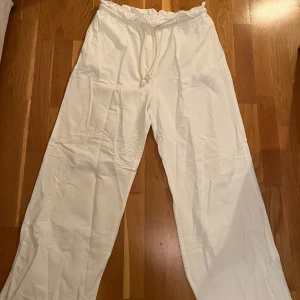 Vita linnebyxor med snörning från HM - Säljer ett par vita linnebyxor med bred passform och dragsko i midjan. Byxorna har en avslappnad look och är perfekta för varmare dagar. De är tillverkade i ett lätt och luftigt linnematerial och har raka ben. Storlek M. 