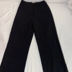 Svarta vida/raka kostymbyxor - Stilrena svarta kostymbyxor med rak och vid passform. Perfekta för en clean och trendig look. Byxorna har klassisk midja och är tillverkade i ett mjukt tyg som ger en snygg siluett.