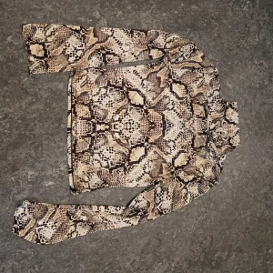 Beige långärmad topp med ormmönster - Säljer en snygg långärmad topp från Bershka med beige och brunt ormmönster. Tight passform och stretchigt material som sitter skönt på kroppen. Perfekt för dig som vill sticka ut med ett trendigt djurmönster.