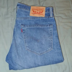Levi's 511 ljusblå jeans W32 L34 - Säljer ett par klassiska Levi's 511 jeans i ljusblå tvätt. Modellen är slim fit med raka ben och normal midja. Jeansen har fem fickor, ikonisk röd Levi's-tagg och patch bak i midjan. Perfekta för en avslappnad och stilren look. Aldrig andvända och i väldigt fint skick, inget som helst slitage i skrev eller knän.