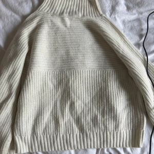 Vit stickad polotröja med struktur - Säljer en vit stickad polotröja med grov ribbad struktur och hög krage. Tröjan har lång ärm och är perfekt för lager-på-lager. Enkel och stilren design som passar till allt.