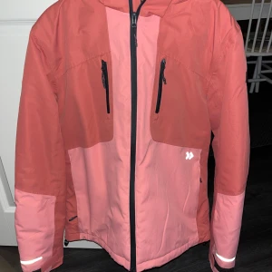 Skidkläder - Säljer ett par snygga täckbyxor i två nyanser av rosa med svarta detaljer och förstärkningar vid bensluten. Byxorna har praktiska hängslen, dragkedjor vid fickorna och justerbar midja. Perfekta för vinterns alla äventyr i snön. Även en jacka som matchar till. Använda under en skidresa och har inga defekter. Jacka i S och byxor i M.