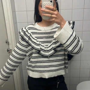 Randig stickad tröja med volang - Säljer en vit och svart stickad tröja med breda ränder och snygga volangdetaljer över axlarna. Tröjan har lång ärm, rund halsringning och är riktigt mjuk och skön. Perfekt för dig som gillar en trendig och unik look. Den ör från h&m och är i storlek L men passar som S använt två gånger iprincip helt ny  