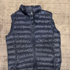 Svart dunväst från Uniqlo - Snygg svart dunväst från Uniqlo i storlek S. Västen är quiltad med horisontella sömmar, har hög krage och dragkedja framtill. Lättviktig och vattenavvisande, perfekt för lager-på-lager-stil under kyliga dagar.