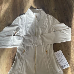 Lululemon define jacket  - Supersnygg vit Define Jacket från Lululemon med guldfärgade dragkedjor, figurnära passform och hög krage. Storlek 2 