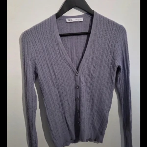 Ljuslila kofta från Zara med pärlknappar, M - Supersöt ljuslila kofta från Zara med kabelstickat mönster och dekorativa pärlknappar. V-ringad och figurnära passform, perfekt att styla med jeans eller kjol. Långärmad och mjuk i materialet, känns både trendig och klassisk.