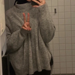 Grå oversized polotröja H&M - Mysig grå polotröja från H&M i oversized modell. Tröjan har hög krage, långa ärmar och är stickad i ett mjukt material. Enkel att matcha med jeans eller leggings.