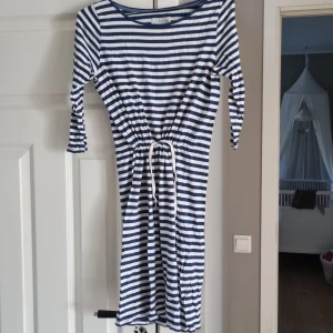 Randig klänning från Lexington - Snygg randig klänning från Lexington i marinblått och vitt. Modellen har trekvartsärm, dragsko i midjan och är tillverkad i mjuk bomull. Perfekt för en avslappnad och stilren look.