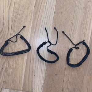 Svarta flätade armband i läderlook - Tre svarta armband med justerbar knytning. Två av armbanden har flätad design och ett har en slätare yta med lindade detaljer. Perfekta för en cool och avslappnad stil.