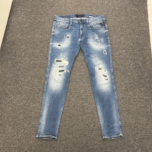 Blå slitna skinny jeans Replay - Säljer ett par ljusblå Replay Anbass med slitningar och hål på framsidan. Jag säljer jeansen pga att de har blivit lite små för mig som syns på bilden. Har ni frågor så tveka inte med att ställa de! Priset är ej hugget ur sten!