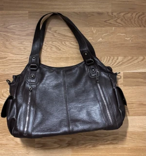 AYVA BROOKLYN BAG - Ayva brooklyn bag i färgen Coffee (mörkbrun) Nyskick, aldrig använd. Medföljer ett längre band. 40x25x15. Perfekt som skolväska då både dator och böcker får plats! 