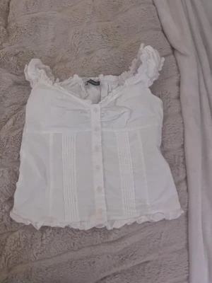 Vit blus med volang och knappar - Supersöt vit blus från brandy använd ändrat 1-2 gånger och har inga defekter! Ny pris 280kr 