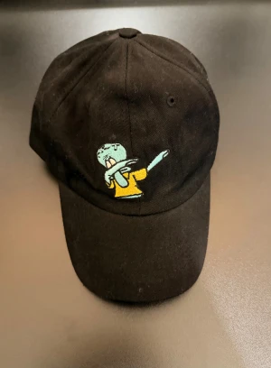 Svart keps med Squidward broderi - Svart keps i 100% bomull med broderad Squidward som dabbar på framsidan. Hojta till vid behov av flerbilder eller om frågor!