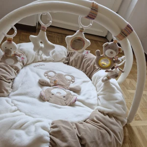 Babygym mjuk lekmatta med hängande leksaker - Mysig babygym från BabyFehn i beige och vitt med mjuk lekmatta och hängande gosedjur. Perfekt för lek och stimulans för små barn. Inga synliga fläckar eller skador, ser mycket välvårdad ut. Passar både pojke och flicka. Hämtas i norsborg botkyrka eller fraktas så fort så möjligt pågrund av flytt. Knappt använd. 