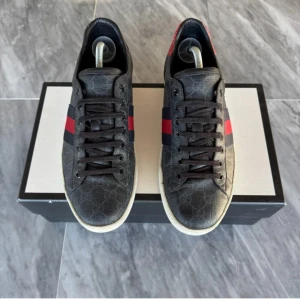 Gucci sneakers med GG-mönster - Snygga Gucci sneakers i svart med klassiskt GG-monogram, röda och marinblå ränder på sidorna och olika färg på hälarna – en röd och en lila. Mitt pris 2100kr nypris 6000kr. Storlek 44 passar även 45.