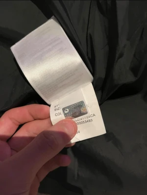 Svart dunjacka från Canada Goose - Svart dunjacka från Canada Goose med huva och avtagbar pälsdetalj. Jackan har ett broderat märke på ärmen, dragkedja och knappar framtill samt quiltad design. Perfekt för kalla dagar och har en clean, stilren look som funkar till streetwear.