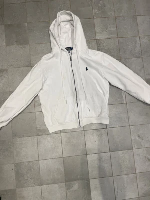 Vit hoodie från Polo Ralph Lauren - Vit hoodie från Polo Ralph Lauren i custom fit med dragkedja framtill och klassisk huva med snörning.