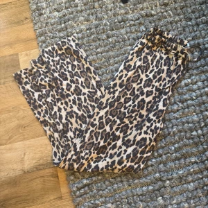 Leopardmönstrade wide byxor Gina Tricot - Snygga wide byxor från Gina Tricot med leopardmönster i beige och bruna toner. Byxorna har resår i midjan för skön passform och är tillverkade i mjukt material som känns lätt mot huden. Perfekta för dig som vill sticka ut med ett djuriskt print.