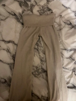 Beige ribbade mjukisbyxor Gina Tricot - Supermysiga beige mjukisbyxor från Gina Tricot med bred ribbad midja. Byxorna har en loose passform och är tillverkade i mjukt stickat material som är perfekt för chill dagar. Snyggt och enkelt att matcha med en hoodie eller t-shirt.