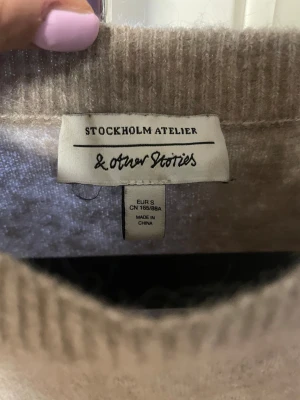 Beige stickad tröja från & Other Stories - Supermysig beige stickad tröja från & Other Stories Stockholm Atelier. Tröjan har en rund halsringning, trekvartsärmar och en loose passform som ger en chill vibe. Perfekt för lager-på-lager under kyliga dagar.