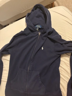 Marinblå hoodie från Polo Ralph Lauren ganska tunn - Snygg marinblå hoodie från Polo Ralph Lauren med klassisk logga broderad på bröstet. Tröjan har huva, dragkedja framtill och två stora fickor. Perfekt för chill dagar och enkel att matcha med jeans eller joggers. Pris kan diskuteras 