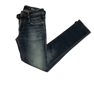 Replay Anbass jeans mörkblå - Snygga Replay Anbass jeans i mörkblå tvätt med slitningar och klassiska fem fickor. Byxorna har raka ben, kontrastsömmar och läderpatch bak i midjan. Perfekt passform och coola detaljer som ger en modern vibe.