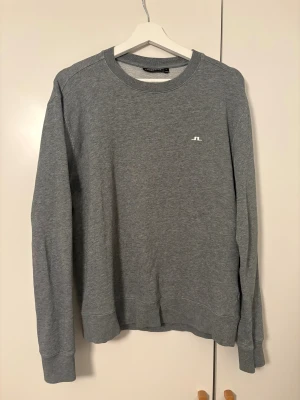 Grå sweatshirt från J.Lindeberg - Snygg grå sweatshirt från J.Lindeberg med diskret logga på bröstet. Tröjan har rund hals, långa ärmar och är tillverkad i mjuk bomull. Perfekt för dig som gillar stilrena och enkla plagg med en sportig touch.