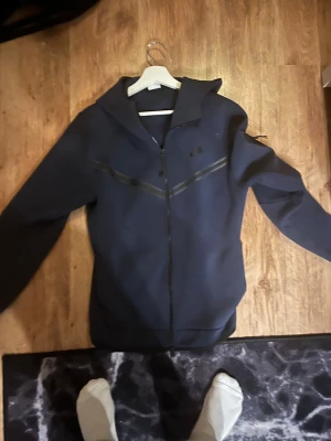 Mörkblå Nike tech med huva - Nike tech hoodie i mörkblått, fräsch hoodie som går att matcha med det mesta. Det är oanvänd då jag fick två likadan när jag fyllde år. 