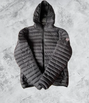 Svart Colmar dunjacka med huva - Säljer en svart dunjacka från Colmar Originals med huva och snygga quiltade detaljer. Jackan har dragkedja framtill och Colmar-logga på ärmen. Perfekt för dig som vill ha en stilren och varm jacka med lätt känsla och cool look.