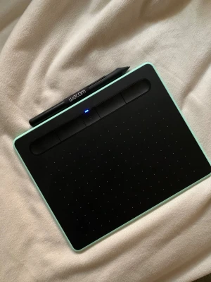 Wacom Intuos Small - Wacom Intuos ritplatta i mintgrönt, komplett med penna och USB-kabel. Plattan är i fint skick med minimalt slitage, och pennan har extra spetsar. Perfekt för digitalt skapande, illustration och retuschering. Enkel att ansluta till datorn via USB. Används bara ett fåtal gånger.