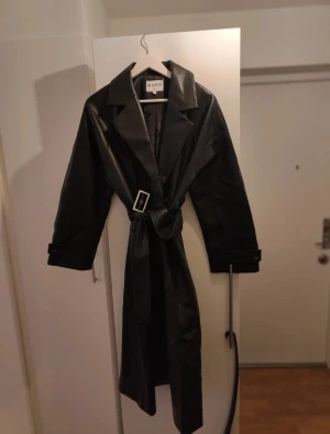 Faux leather coat with belt  - Faux läder kappa med bälte. Aldrig använd. Köpt för 1000 kr. Lite oversized passform så funkar även för storlek 38 eller liknande.