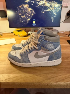 Nike Air Jordan 1 High Hyper Royal - Nike Air Jordan 1 High Hyper Royal i en fräsch mix av ljusblå mocka och vitt skinn, med grå swoosh och detaljer. Klassisk high-top siluett med snörning och perforerad tå för extra stil. Perfekt för dig som vill sticka ut med en ikonisk sneaker. Extremt bra i skick, ser som nya ut. Köpta på stockX för ett par år sedan men har använts ytterst lite, tror inte jag använt dom på 1,5 år! Ingen stress med å sälja så inga skambud tack. Sjukt snygga skor som inte längre passar min stil!