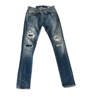  Dondup George  - Snygga blå jeans från Dondup, modell George Skinny Fit. De har slitna detaljer och stora hål på båda benen för en cool, edgy look. Klassisk femficksdesign, knappgylf och tillverkade i jeansmaterial med inslag av bomull och polyester. Mycket bra skick