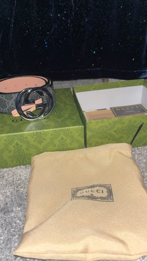 Gucci bälte  - Gucci GG Supreme bälte i svart och grått med klassiskt GG-mönster och stor silverfärgad GG-spänne. Tillverkat i skinn med beige insida. Kommer med originalbox och dustbag. Perfekt accessoar för att lyfta din outfit.