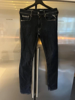 Mörkblå Replay jeans slim fit - Säljer ett par väldigt mörkblå jeans från Replay med snygga kontrastsömmar och klassiska fem fickor. Modellen har smal passform och raka ben, med detaljer som dragkedja på fickan och Replay-lapp bak i midjan. Perfekta för dig som gillar stilrena och moderna jeans.