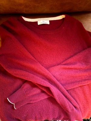 Vinröd Kashmir tröja från Cashmere closet - Mysig vinröd tröja från Cashmere closet i Kashmir. Rund halsringning med kräm vit kantdetalj och långa ärmar. .