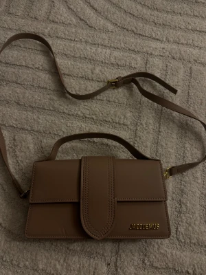 Brun/mörk beige axelväska från Jacquemus - Väska från Jacquemus (fejk!). Använd 1 gång, men har fått defekt. ”Guldet” är lite gult. Inköpt för 600kr 