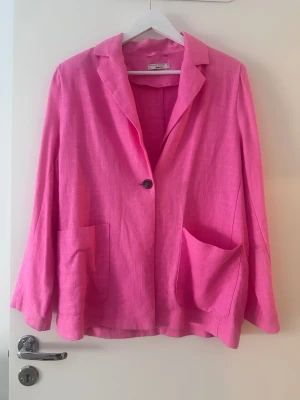 Rosa linnekavaj från By Malene Birger - Snygg rosa kavaj i linne. En knapp framtill och två stora fickor. Perfekt för dig som vill sticka ut med färg och stil. Långärmad och med avslappnad passform.