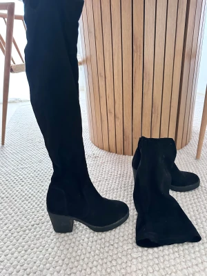 Svarta höga mockastövlar med klack - Säljer ett par svarta, höga stövlar i mjuk mocka med rund tå och stadig klack. Stövlarna har dragkedja på insidan för enkel påtagning och en klassisk, stilren look som passar till många outfits.