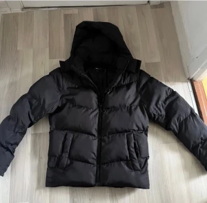 Svart pufferjacka med huva - Svart pufferjacka med huva och dragkedja framtill. Skick 9/10