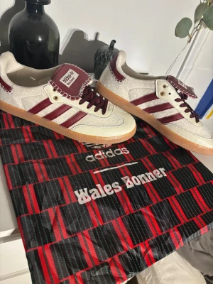 Adidas Wales Bonner Samba HAR MASSA STORLEKAR - Adidas Wales Bonner Samba sneakers i samarbete med Wales Bonner. Snygg design med vinröda och vita detaljer, klassiska tre ränder på sidan och grov gummisula. Ovandel i mocka och skinn, med broderad plös och snörning. Perfekt för dig som gillar unika sneakers.